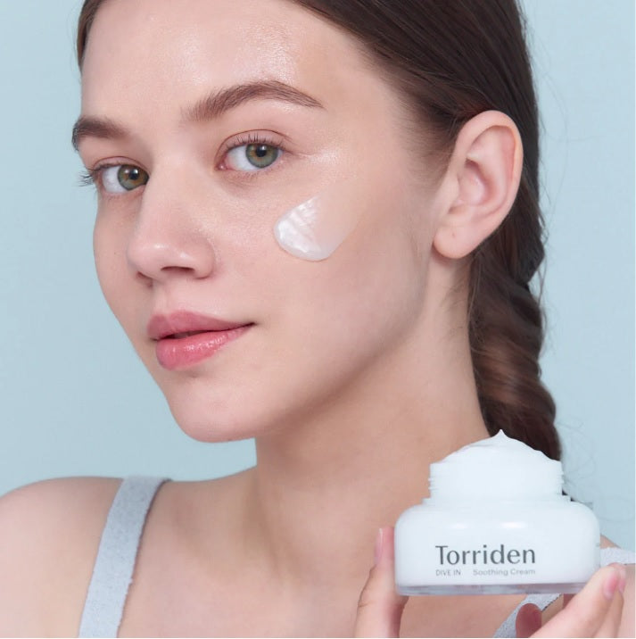 Дівчина тримає відкриту баночку крему Torriden Dive-In Soothing Cream біля шиї, крем нанесений під її оком.