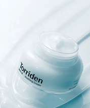 Відкрита баночка крему Torriden Dive-In Soothing Cream стоїть на поверхні, яка нахилена під кутом.