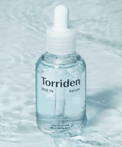 На білій поверхні, покритій водою, стоїть ампула Torriden Dive-In Low Molecular Hyaluronic Acid Skin Serum.