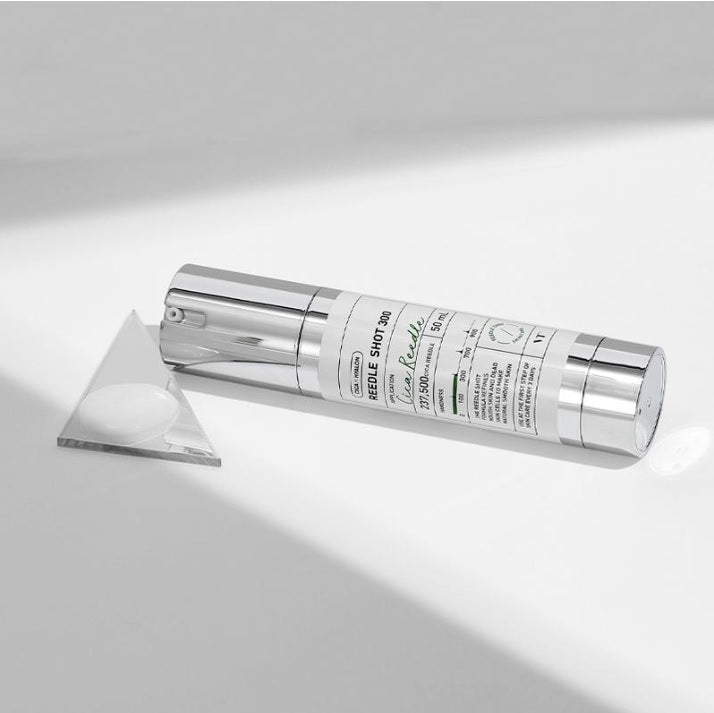 Бустер VT Cosmetics VT Reedle Shot 300 лежить на білій поверхні, поруч — трикутне дзеркальце з нанесеною текстурою засобу.