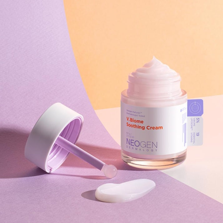 Відкрита баночка крему Neogen Dermalogy V.Biome Soothing Cream стоїть на рожево-оранжевій поверхні, поряд — намазана текстура крему так кришечка.